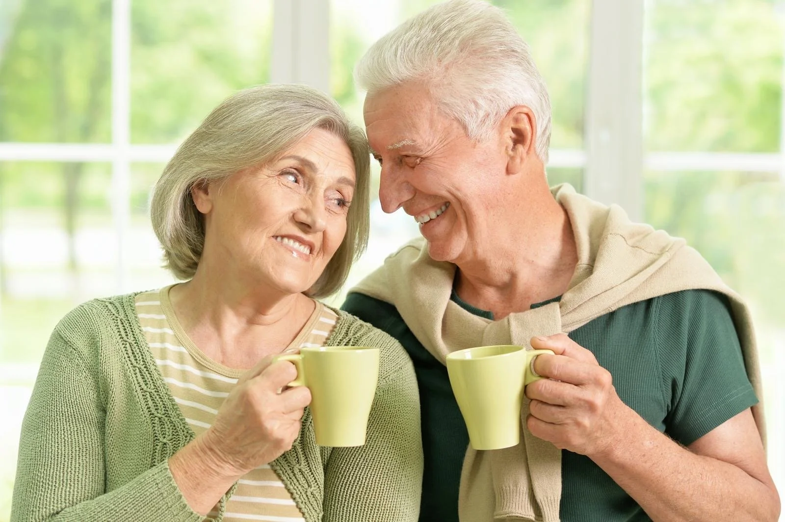 An older couple smiling together over a cup of tea at home